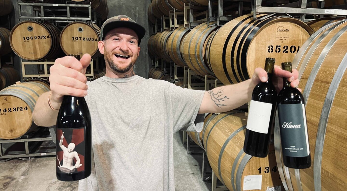 Tyler Williams holding three bottles of wine in the barrel cellar.